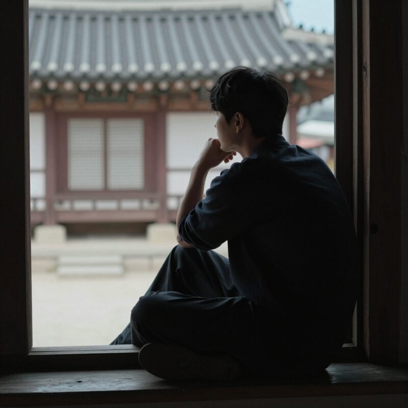 창가에 앉아 멀리 바라보며 생각에 잠긴 사람의 실루엣, 사색적 순간을 상징하는 이미지
