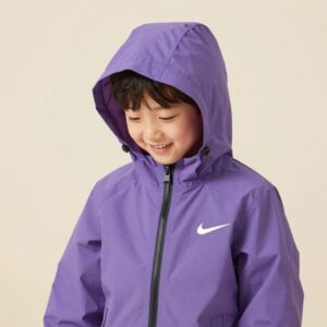 라벤더 컬러의 나이키 키즈 스우시 윈드러너 바람막이를 입은 아이가 밝은 배경에서 웃고 있음