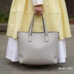 5월 패션 여행룩과 데일리 코디 아이템 테스토니 위저드 34 애쉬 그레이 가죽 토트백이 바닥에 놓여 있고, 연한 라임색 바람막이와 화이트 미니스커트와 함께 코디된 모습