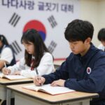 나라사랑 글짓기 대회에서 학생이 책상에 앉아 진지하게 글을 쓰고 있다. 배경에는 태극기와 글짓기 대회 포스터가 보인다.
