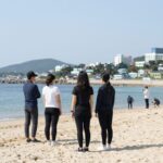 야노 시호 스타일의 래쉬가드를 착용한 여성이 해변에 서 있는 모습. 화이트와 블랙의 조화가 돋보인다.