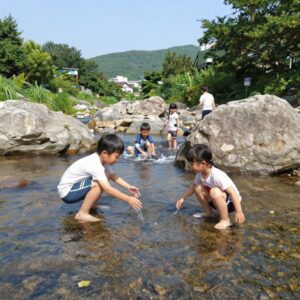 문경계곡펜션 솔수펑이펜션 계곡에서 아이들이 물놀이하는 모습, 맑은 물과 바위가 보인다